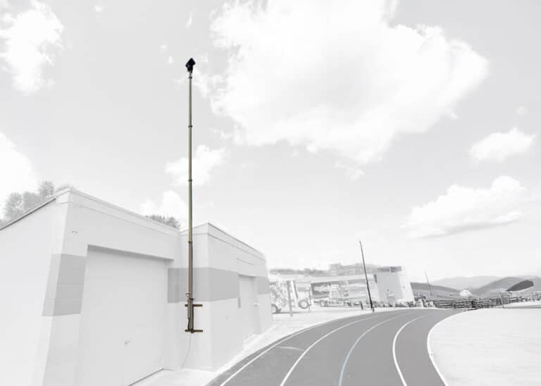 Wall-Mounted Telescopic Mast for Campus Surveillance - Tech Deployments Made Simple by Critical Tech Solutions Grayscale image of wall-mounted pneumatic telescopic mast installed for facility surveillance.