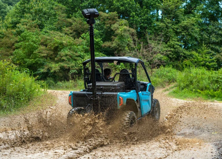 Rear view of a blue UTV driving through muddy terrain with an RQ621 mobile surveillance tower by Critical Tech Solutions mounted on the hitch, equipped with a portable surveillance system in the dump bed.
