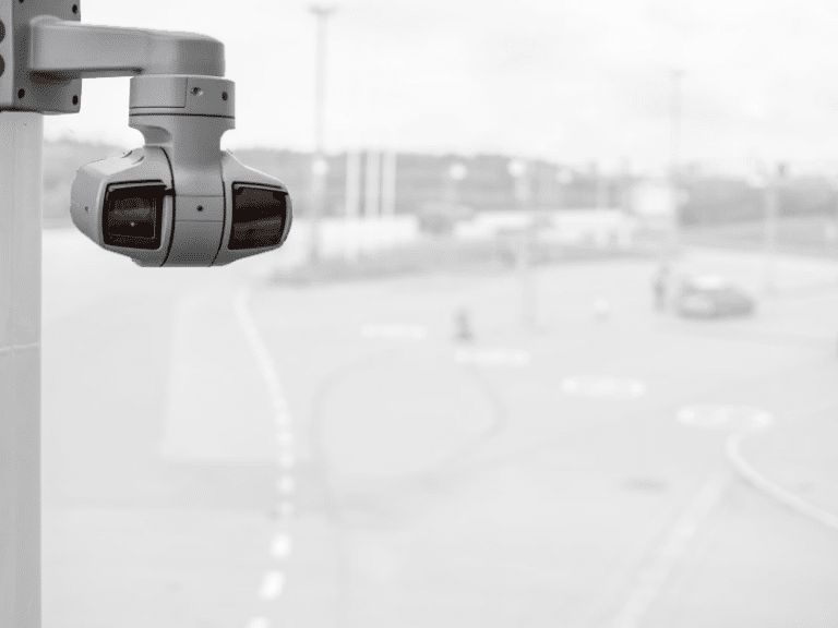 Grey Axis Q6225-LE ptz surveillance camera with wiper hanging upside down on concrete pole monitoring parking lot with blurry background