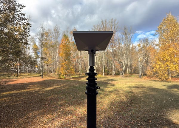 Telescopic mast with mounted Starlink antenna providing internet connectivity in an open field surrounded by autumn trees