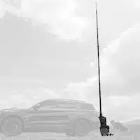Black SUV with an elevated telescopic mast, parked on grassy terrain with mountain ranges and scattered clouds in the distance.
