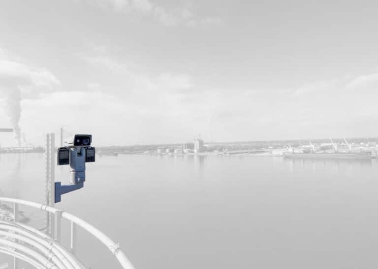 Long-range thermal surveillance camera mounted on elevated railing overlooking industrial port and waterfront